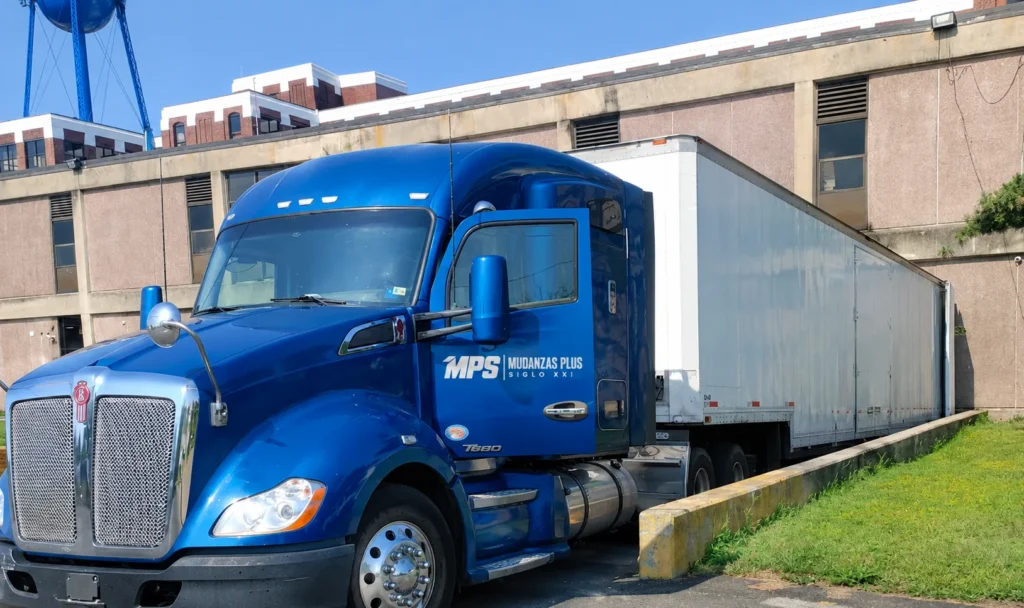 Tráiler azul de Mudanzas Plus Siglo XXI aparcado junto a un almacén